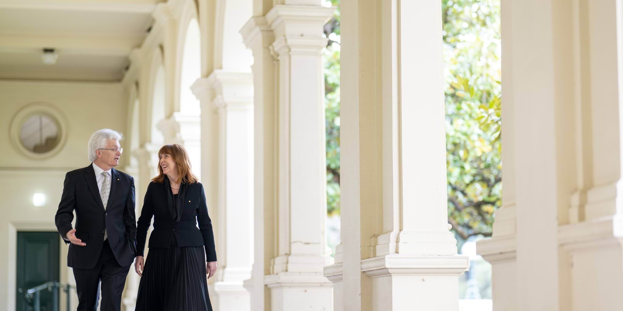 Her Excellency Professor the Honourable Margaret Gardner AC and Professor Glyn Davis AC walking down the colonnade at Government House Victoria.